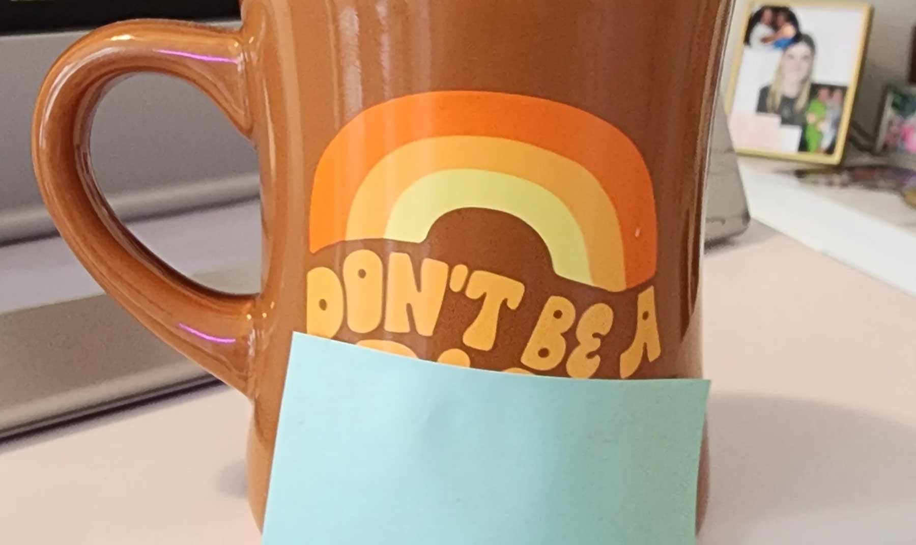 Coffee Mug that says "Don't be a …" (last word is covered by post-it note)