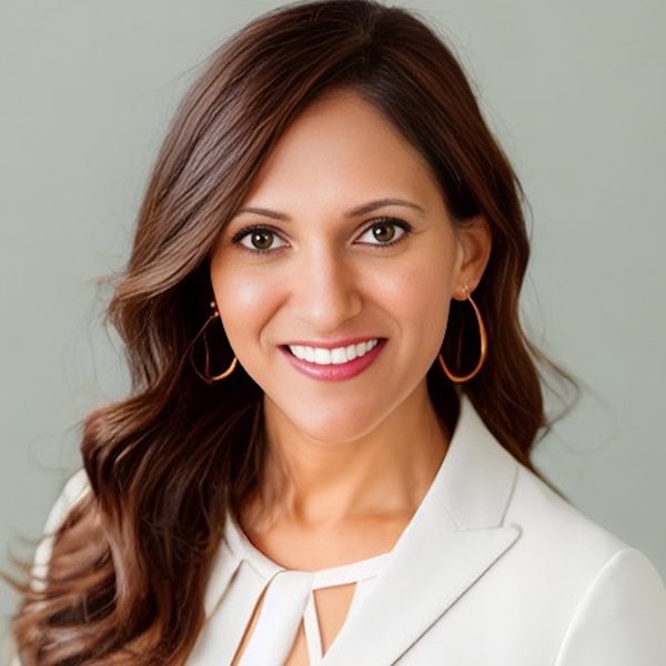 Headshot of Anjali Bindra Patel, a South Asian woman smiling with wavy brown hair and an ivory suit jacket