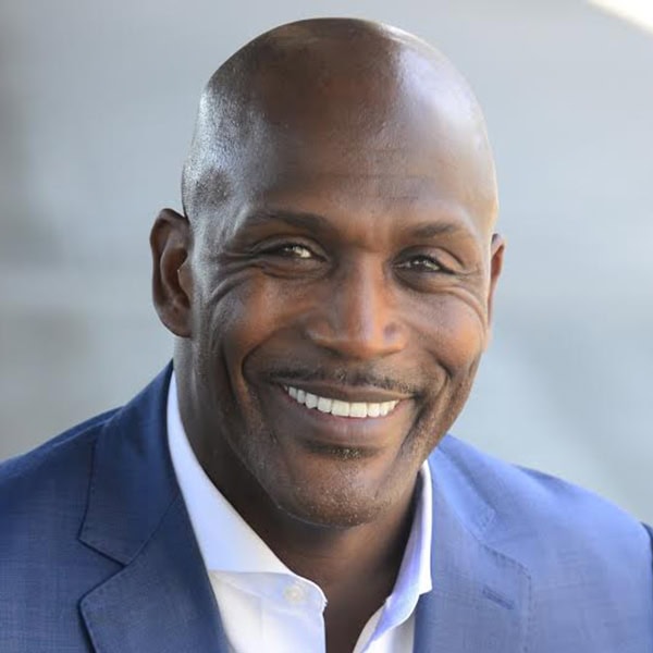 Headshot of Eric Boles, a black man smiling with shaved head, white shirt, and blue suit jacket.